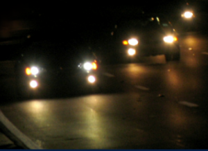 W ciemności widać jadące samochody z włączonymi światłami.