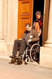 kobieta sprowadza mężczyznę na wózku ze stopnia przed drzwiami wejściowymi ratusza