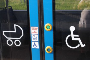 Drzwi krakowskiego tramwaju, na szybach duże białe symbole wózka inwalidzkiego i wózka dziecięcego.